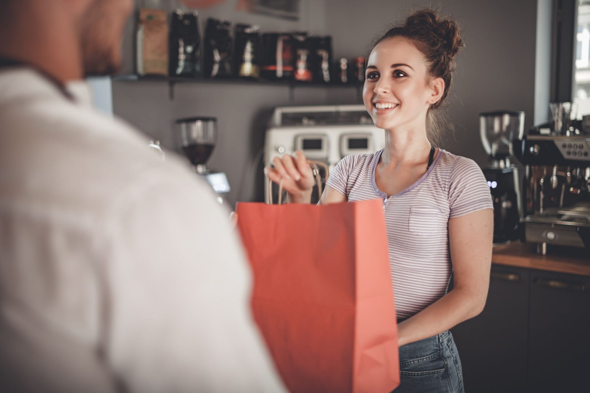 A woman is giving a red bag to a man in a coffee shop.
