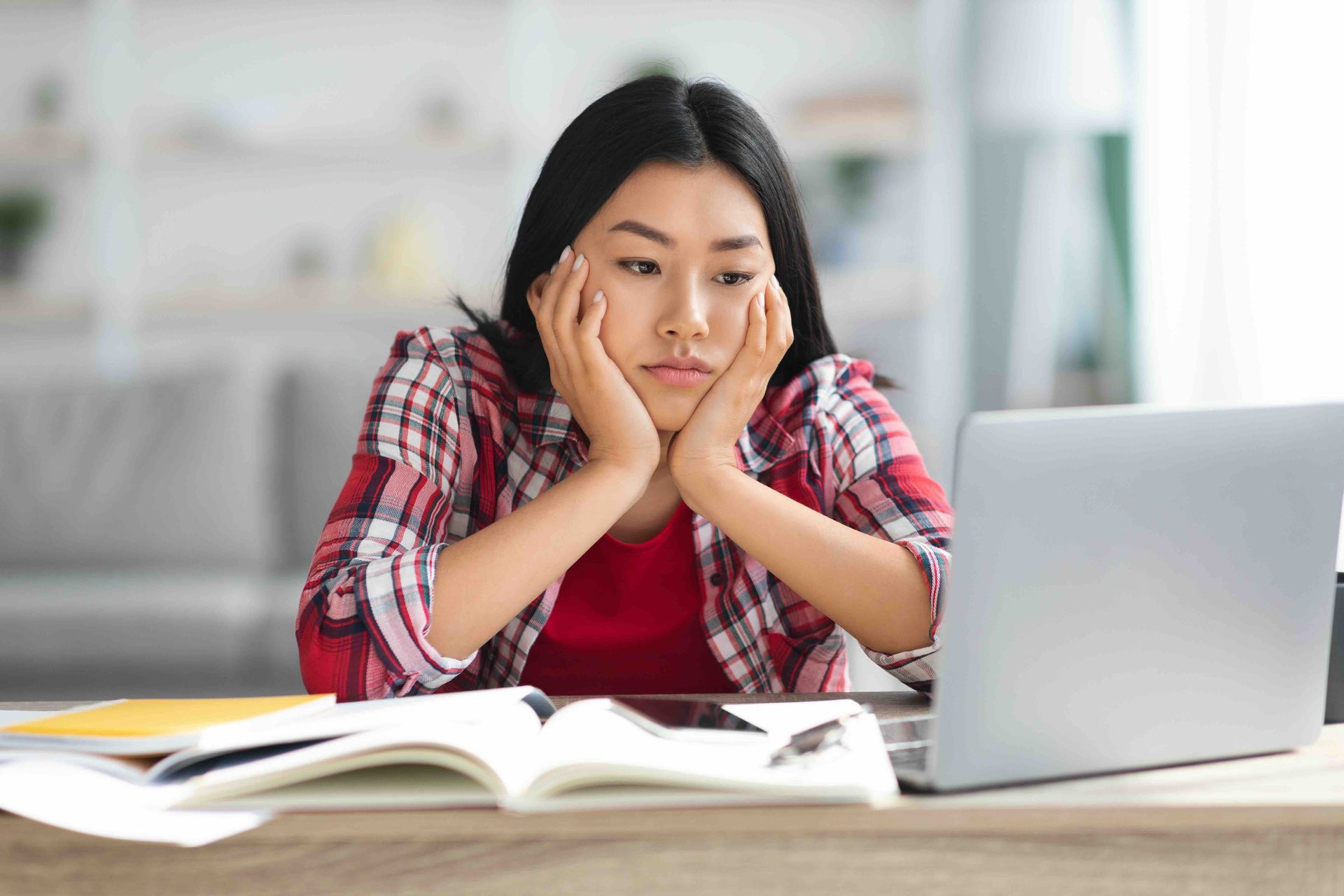 A woman is sitting at a desk with a laptop and books.