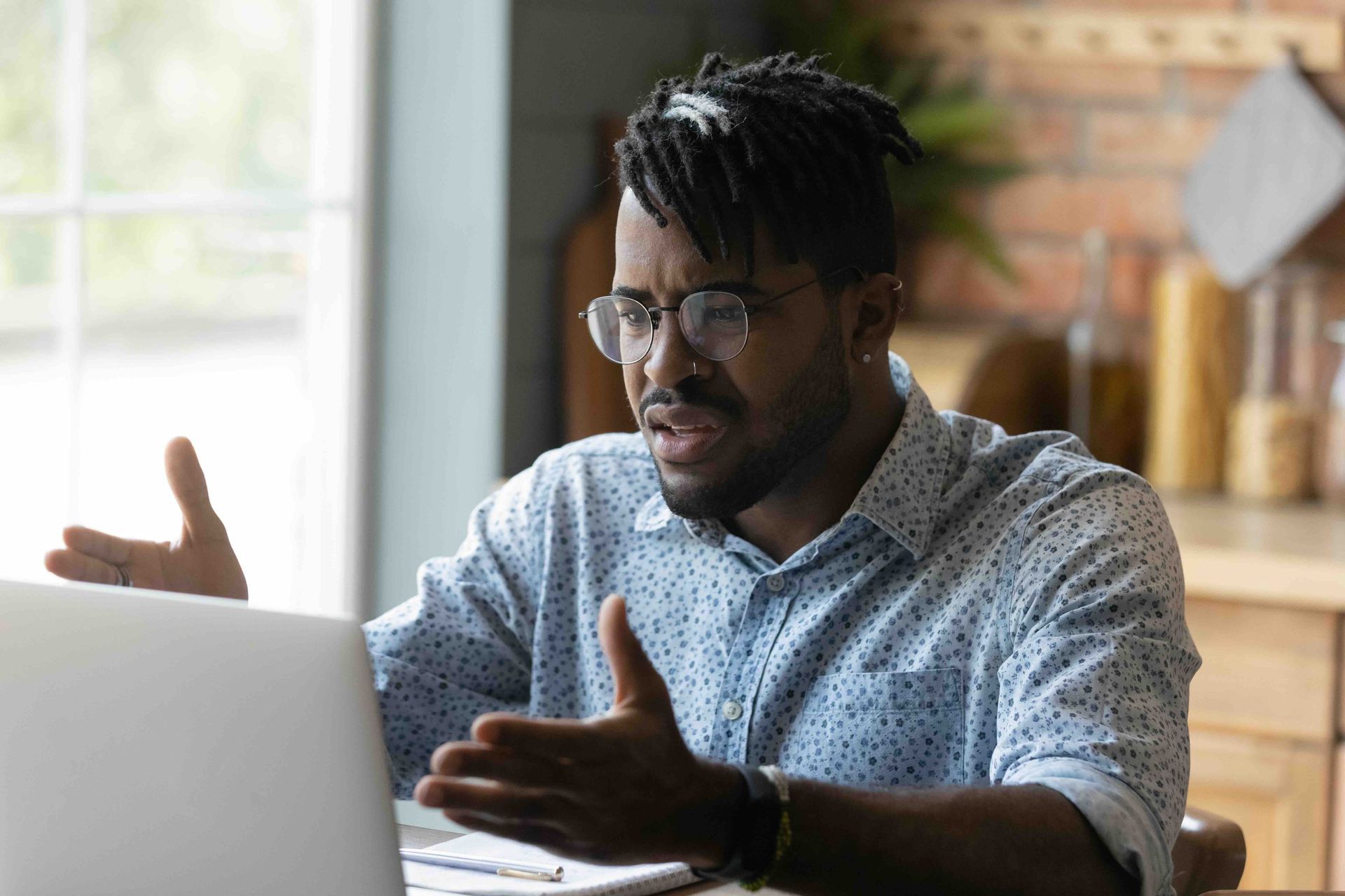 A man wearing glasses is sitting at a table using a laptop computer.