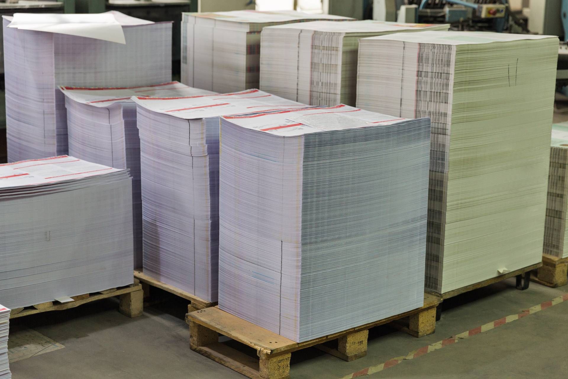 A warehouse filled with lots of stacks of paper on wooden pallets.