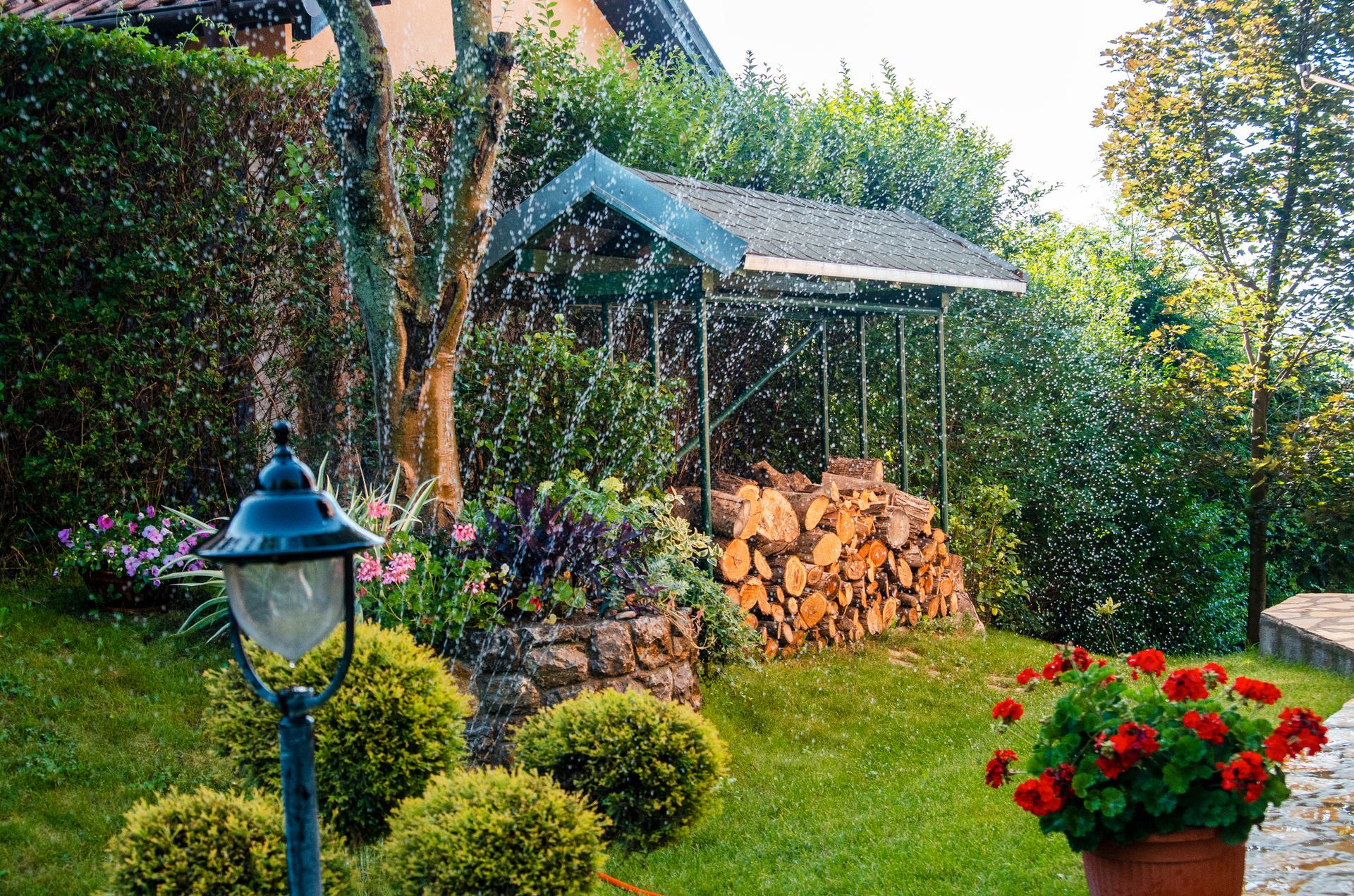 A garden with a lot of plants and flowers and a lamp post in the foreground.