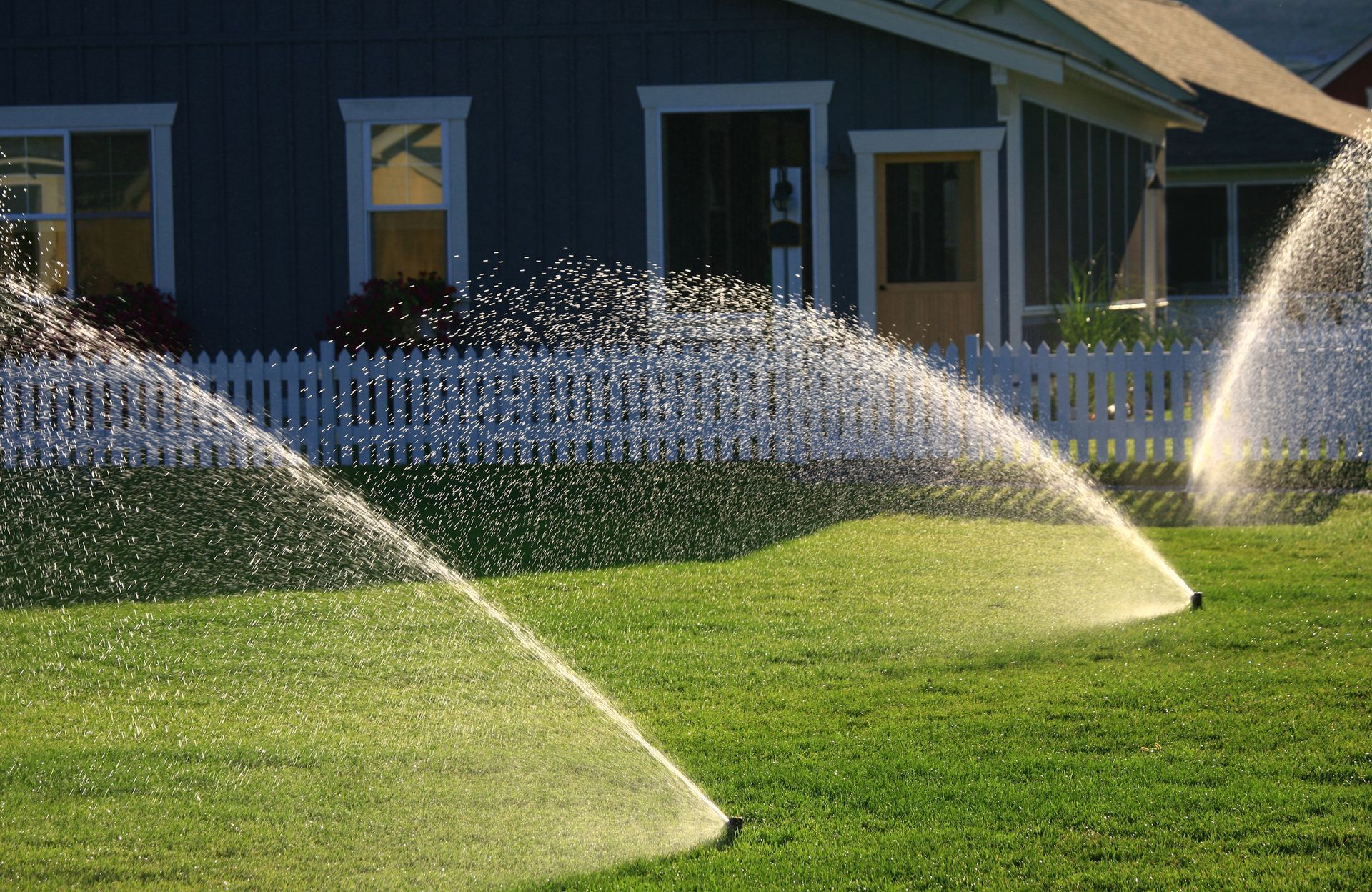 Two sprinklers are spraying water on a lush green lawn in front of a house.