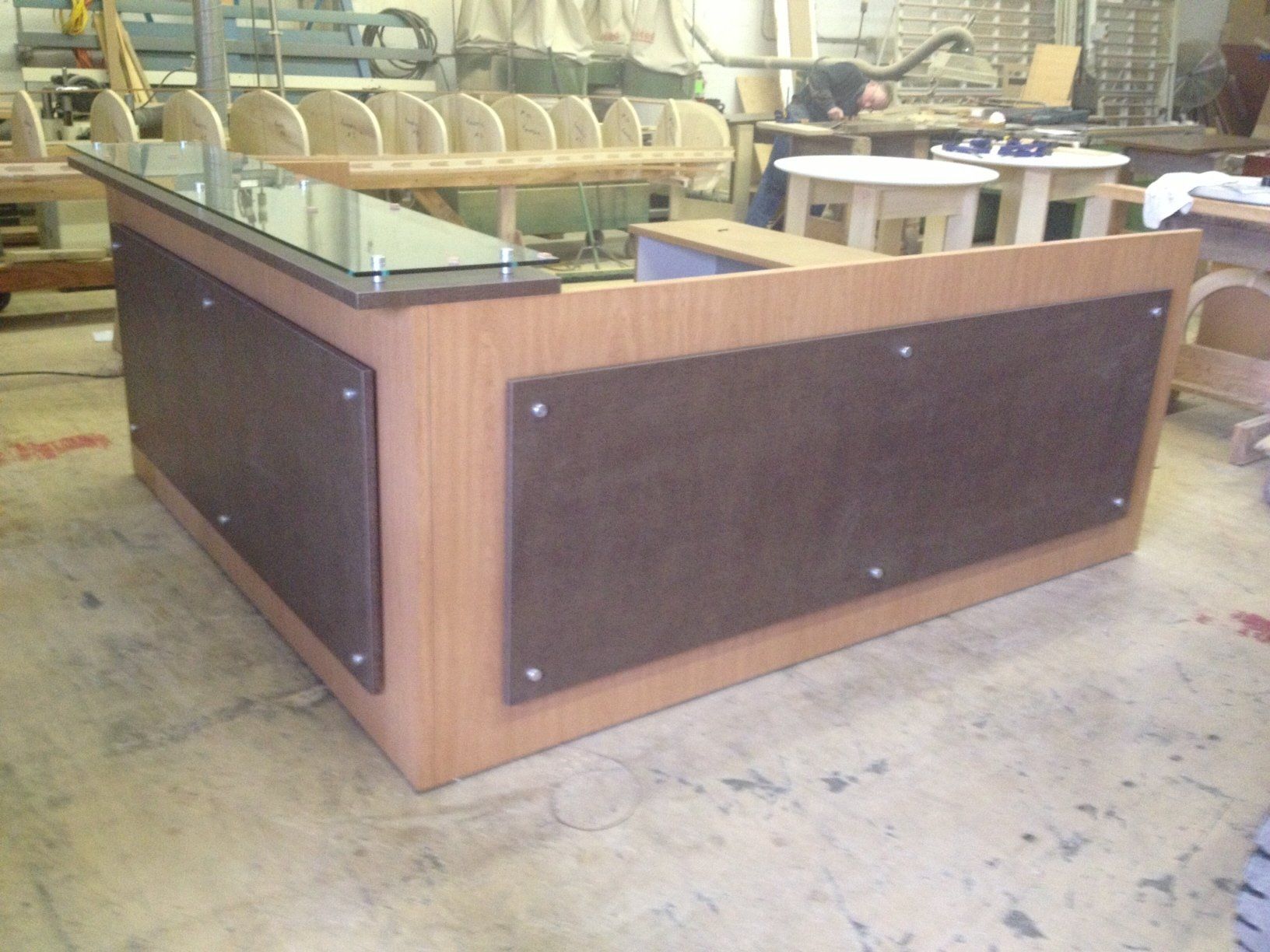 Wooden reception desk with glass top and brown panels, in a workshop.