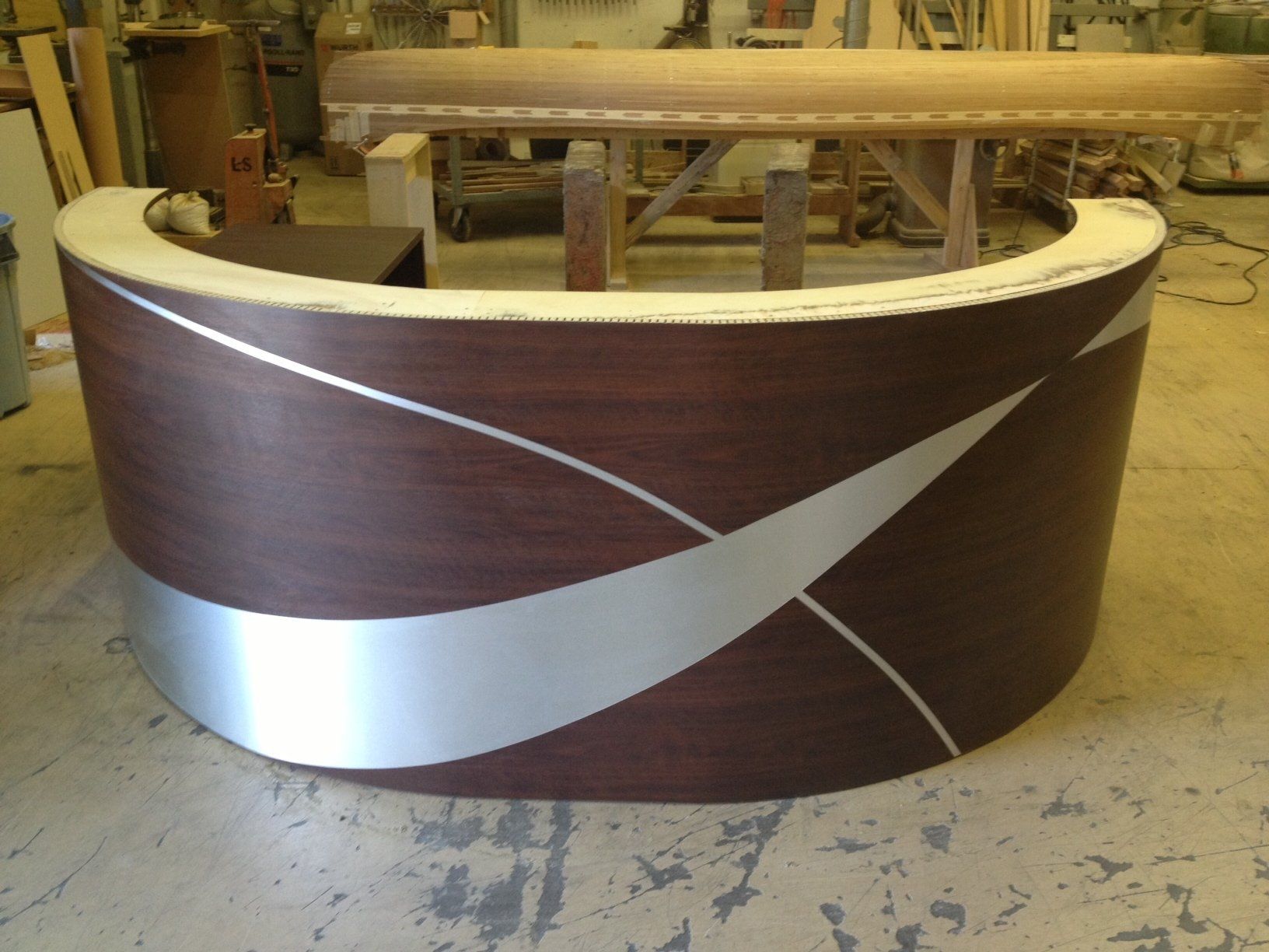 Curved brown reception desk with silver accents, in a workshop setting.