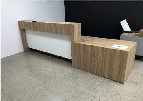 A modern, light wood and white office reception desk against a black and white wall.