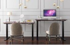 Two brown desks with black legs, chairs, and a computer in front of a white wall.