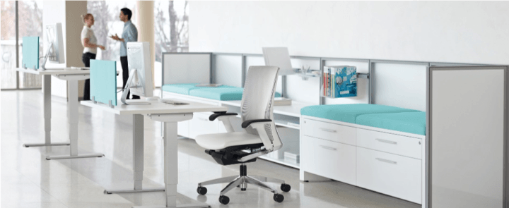 Modern office space with white desks, teal accents, and two people standing near a window.
