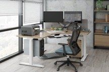 Office desk with two monitors, a printer, and an ergonomic chair by a window.
