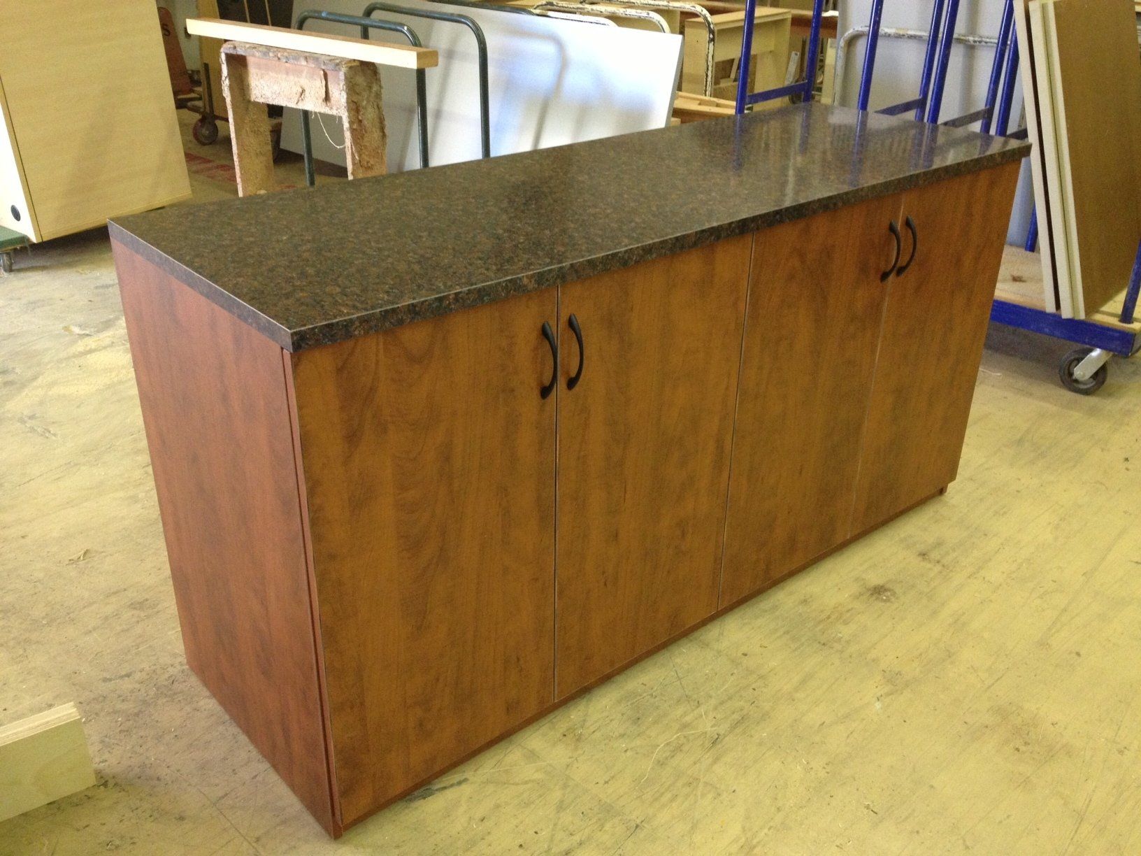 Brown cabinet with dark speckled countertop and black handles, in a workshop.
