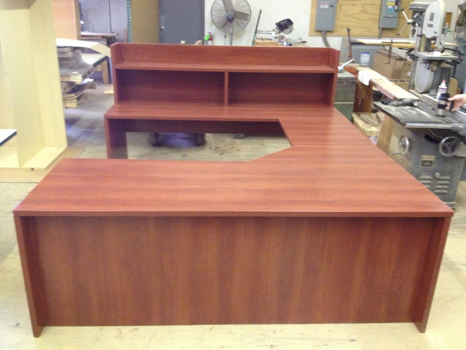 L-shaped wooden office desk with a hutch, in a workshop setting. Red-brown color.