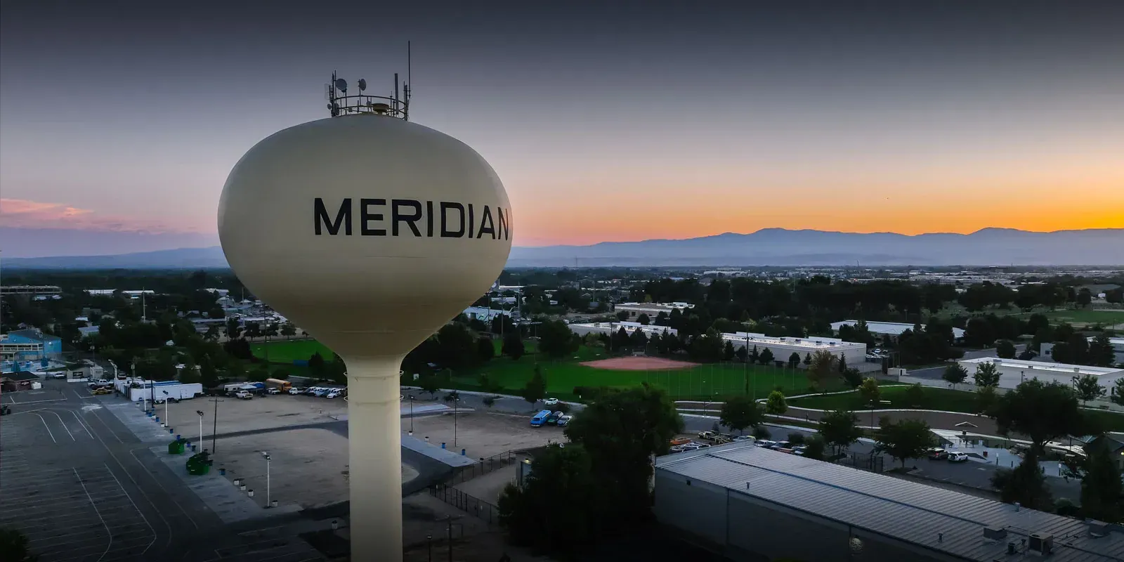 Meridian water tower at sunset with cityscape and mountains in the background.