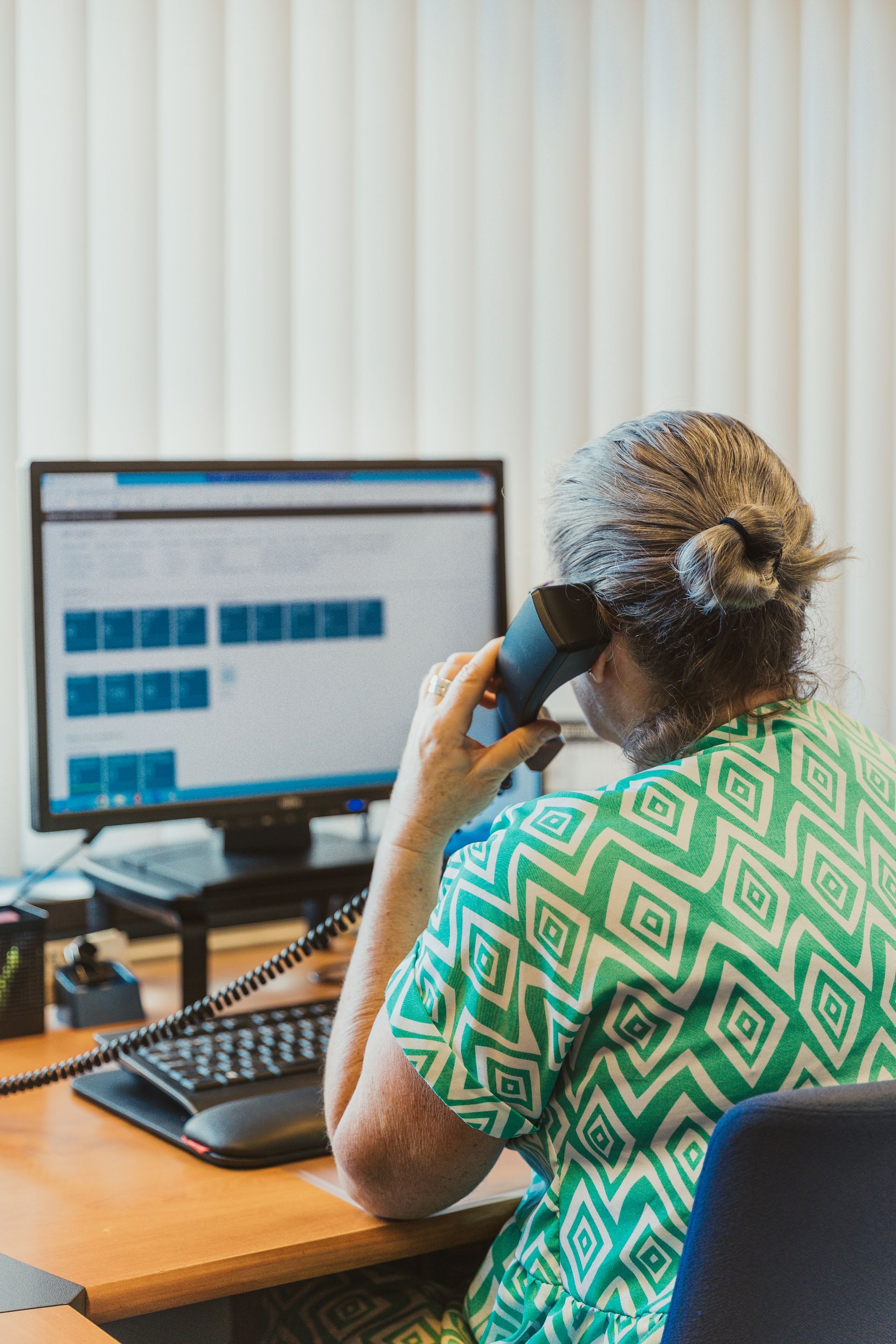 Een vrouw zit aan een bureau en praat via een telefoongesprek achter een computer.