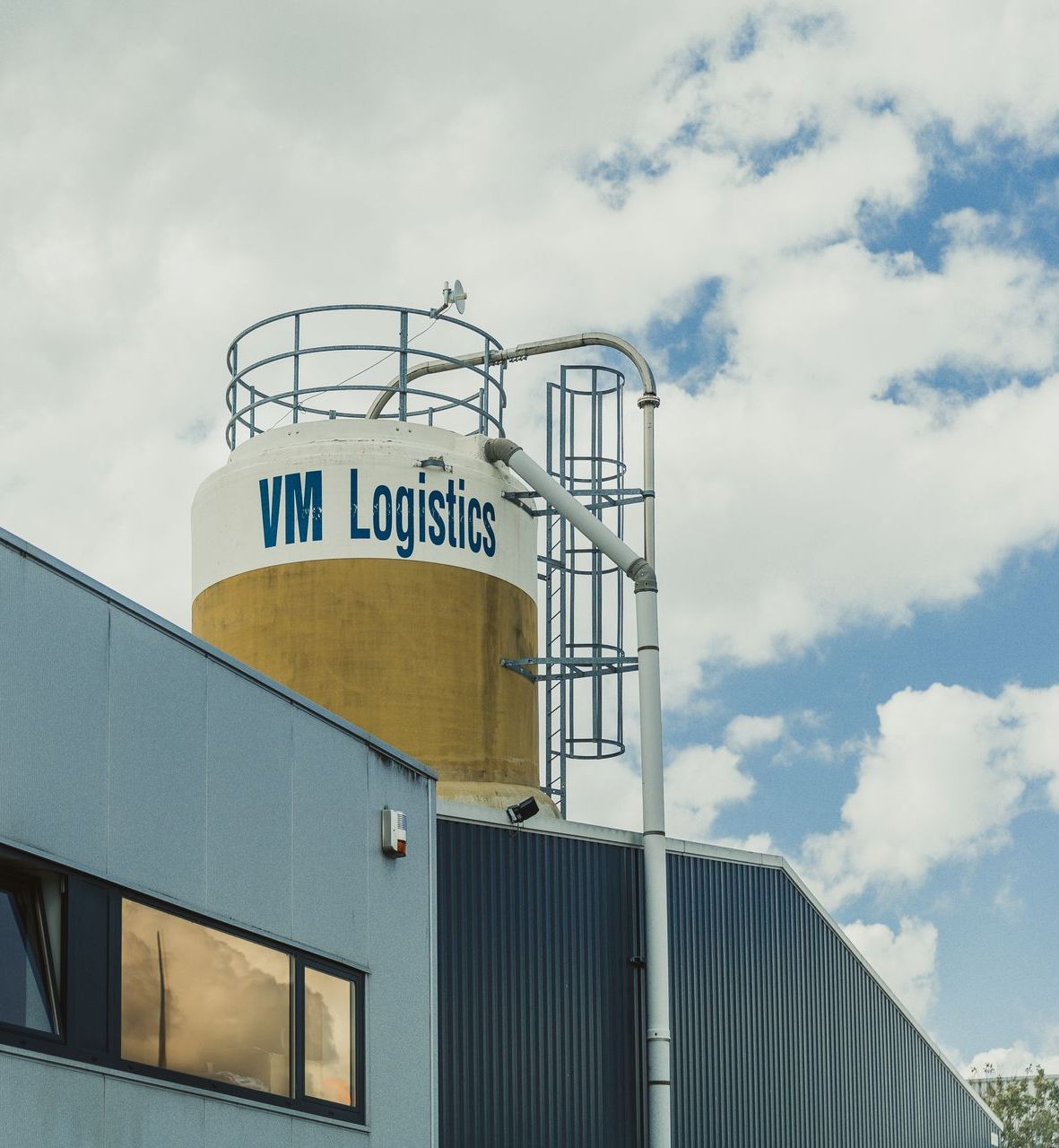 Een gebouw met een silo erbovenop met de tekst vm logistics