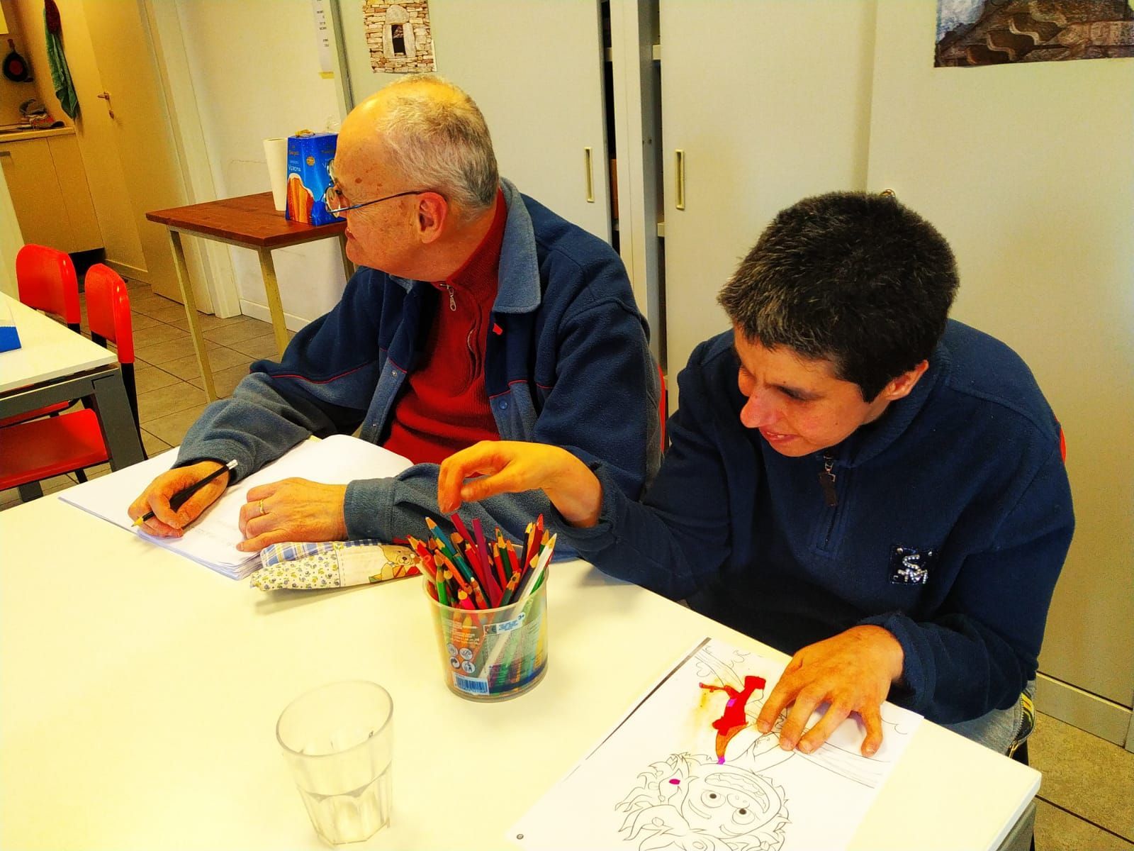 Due uomini sono seduti a un tavolo con una tazza di matite colorate