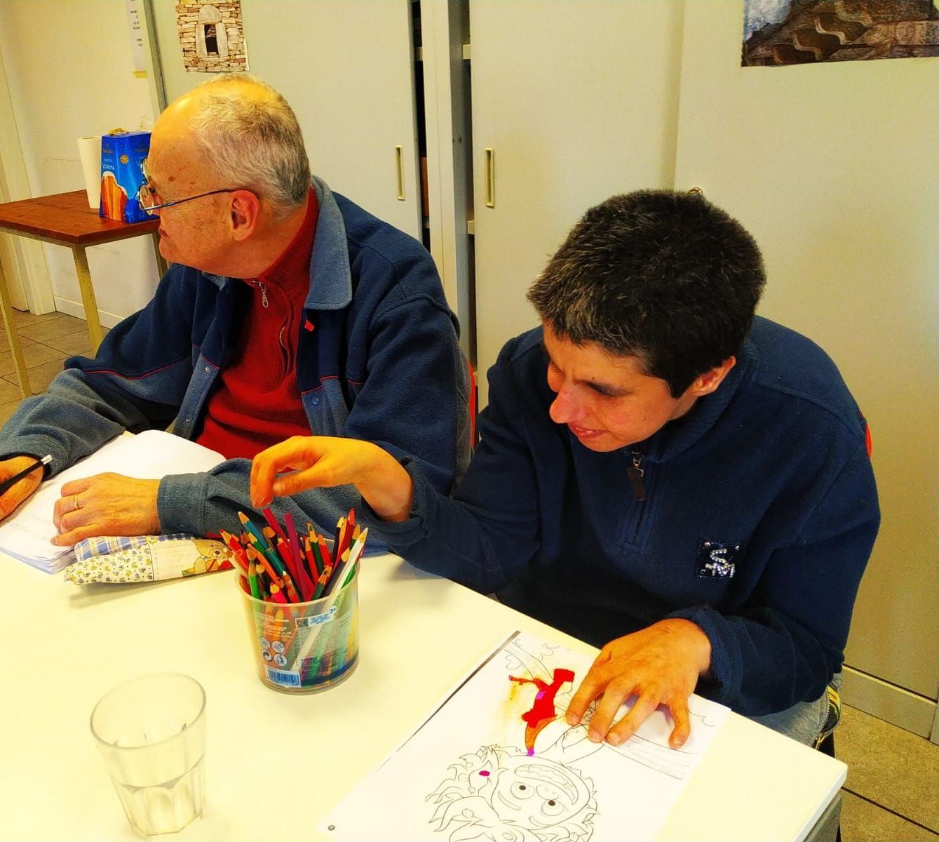 Due uomini si siedono a un tavolo con sopra una tazza di matite colorate