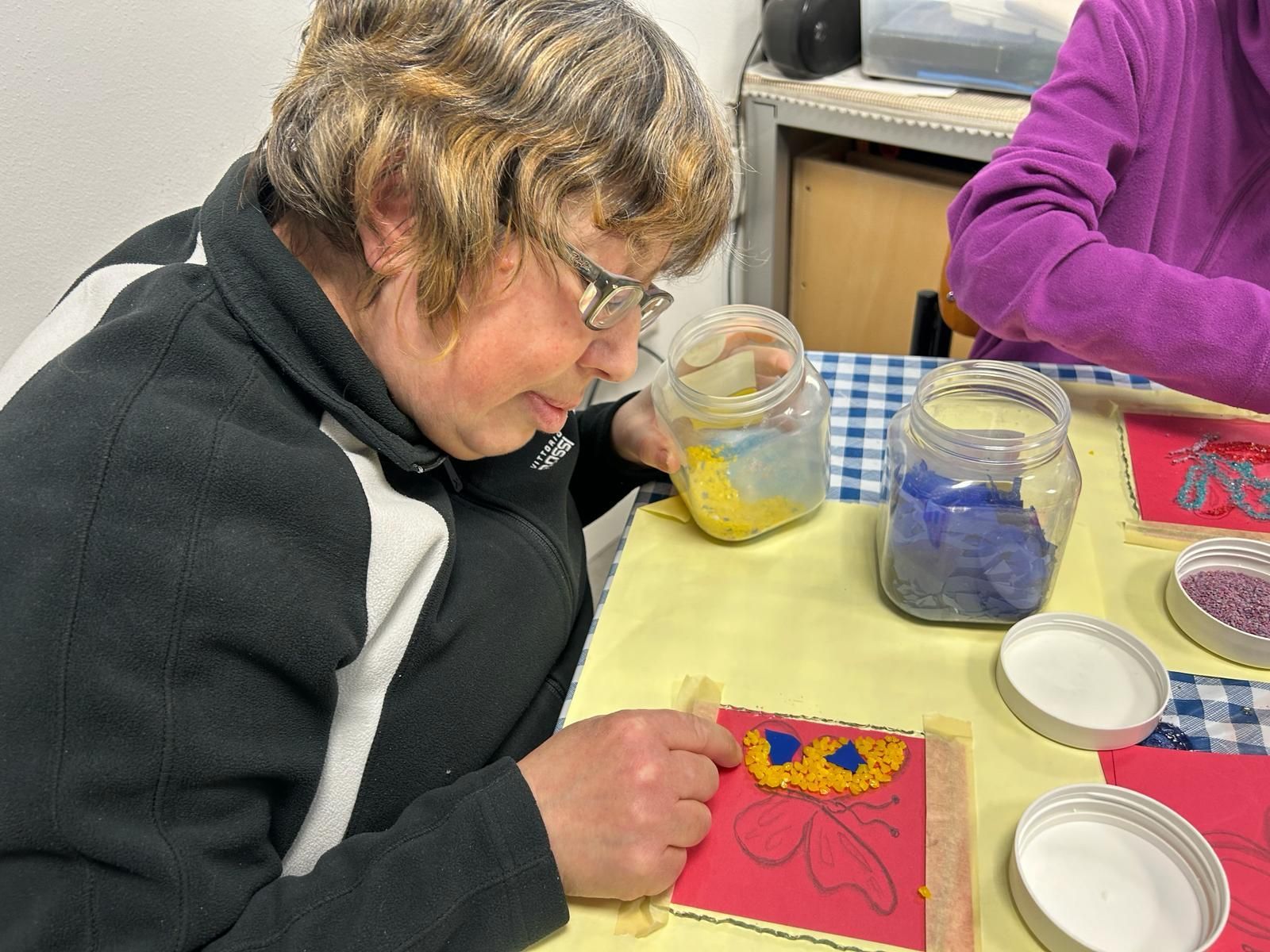 Una donna è seduta a un tavolo e dipinge un quadro con un barattolo di vernice.