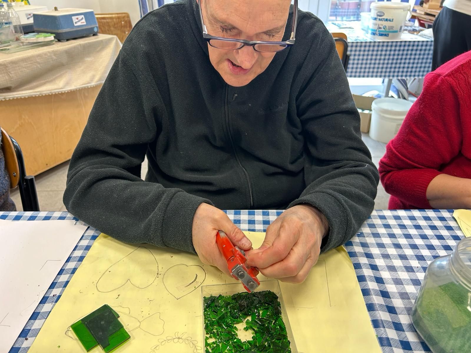 Un uomo è seduto a un tavolo e taglia un pezzo di vetro verde