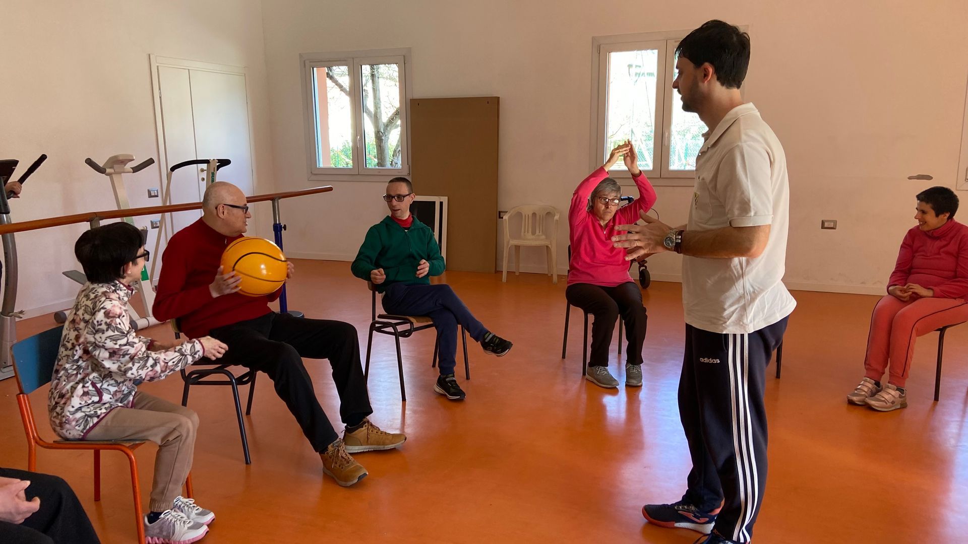 Un gruppo di persone è seduto su delle sedie in una stanza con un uomo in piedi al centro.