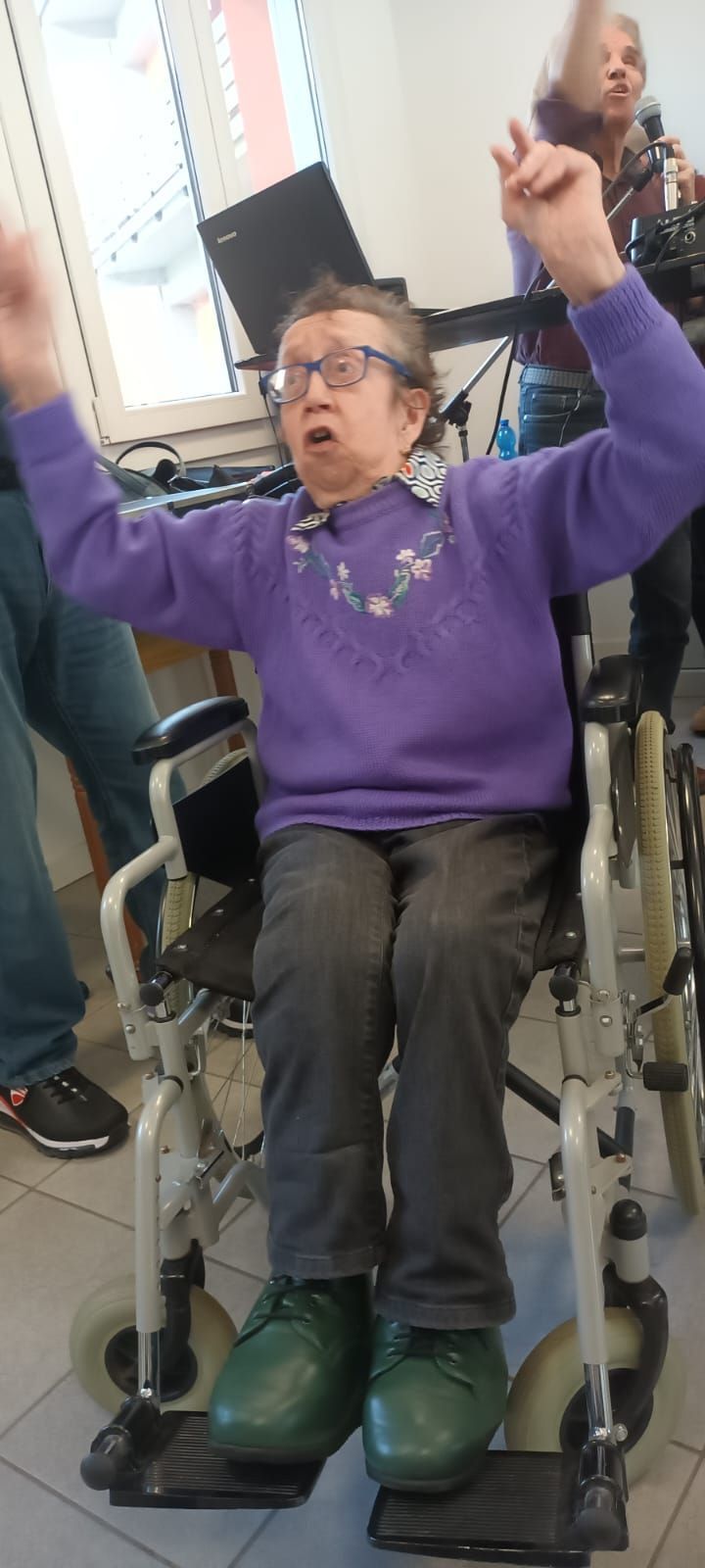 Una donna anziana è seduta su una sedia a rotelle con le braccia alzate.