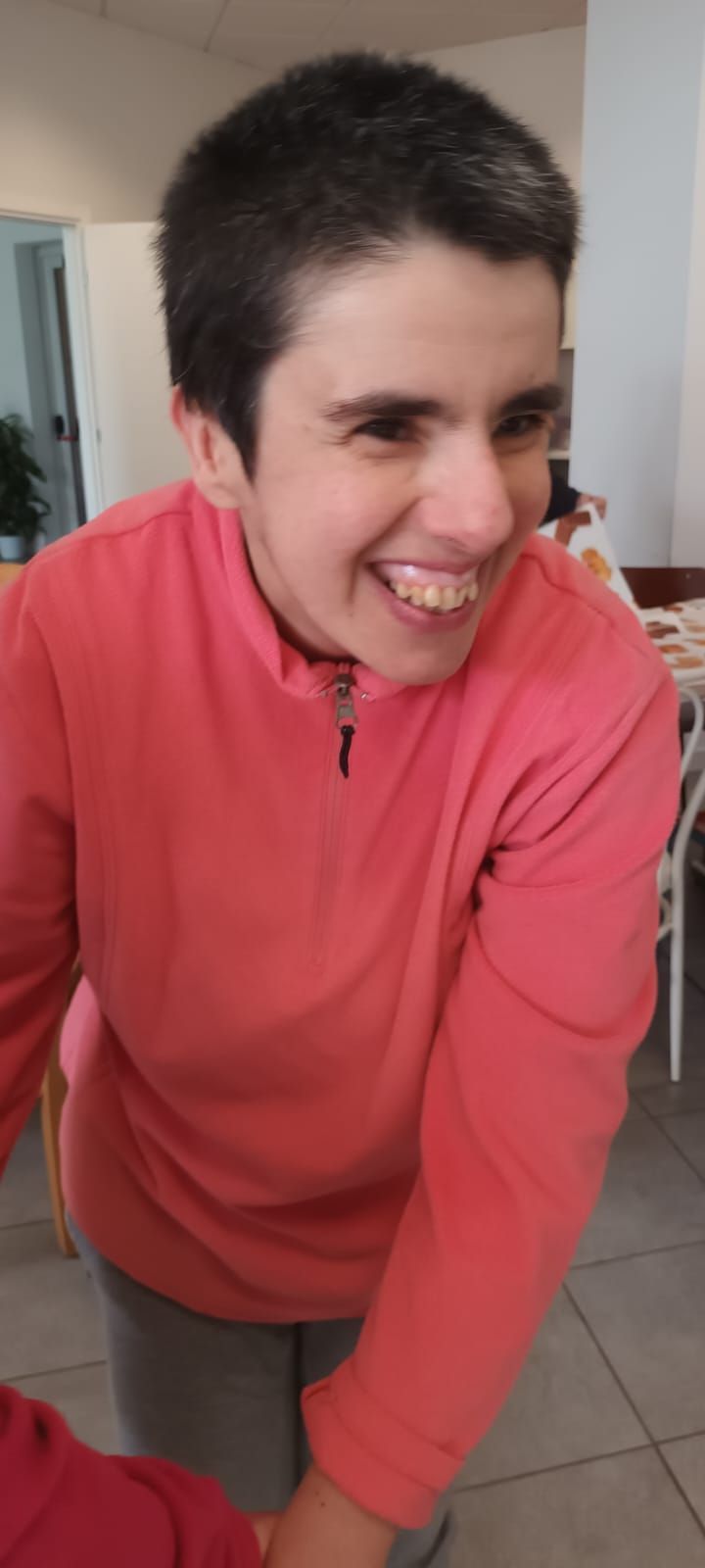 Una donna con un maglione rosa sorride in una stanza.