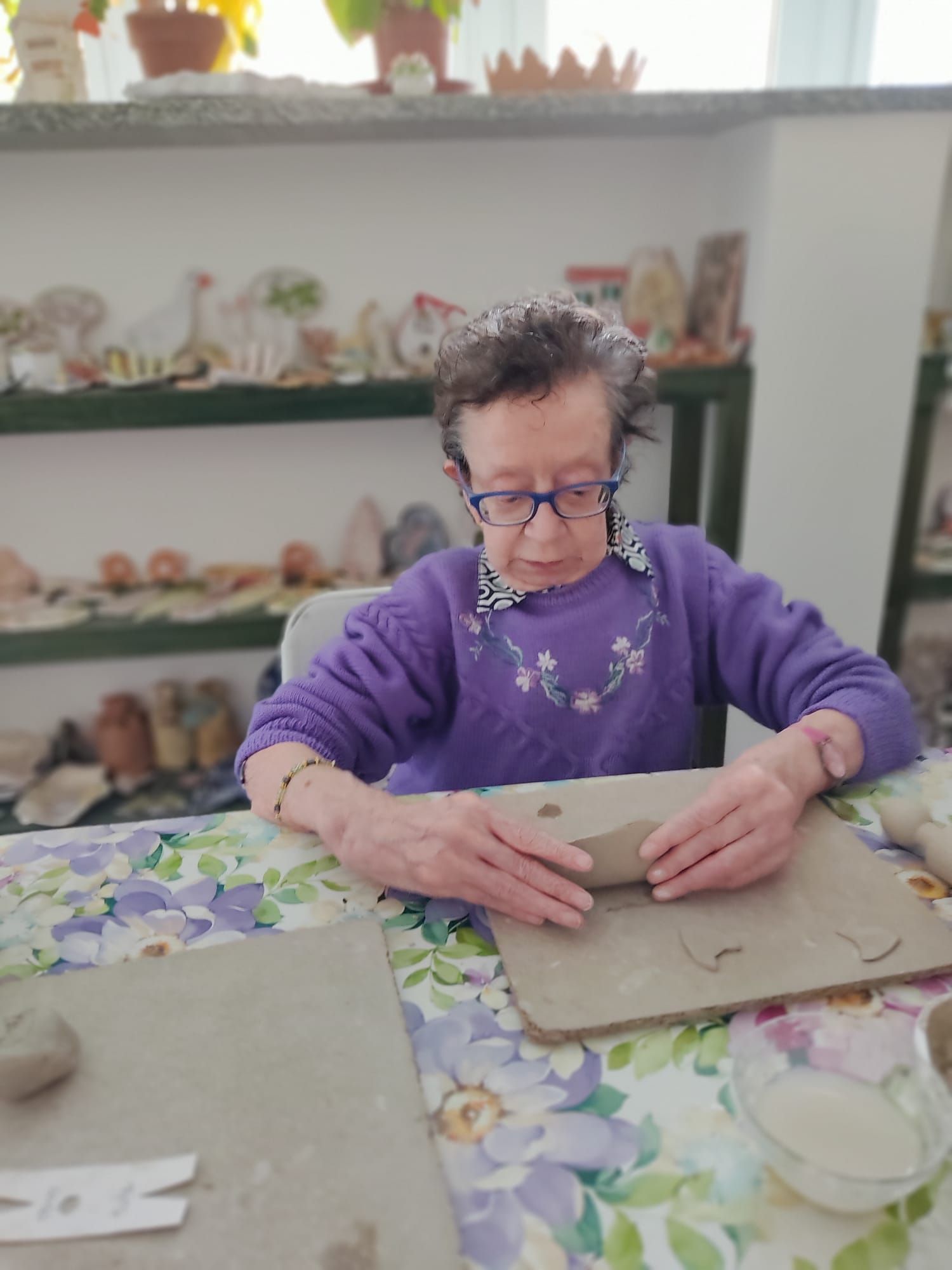 Una donna con un maglione viola è seduta a un tavolo e realizza sculture in argilla.