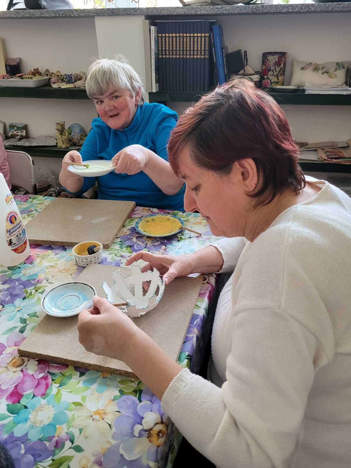 Due donne sono sedute a un tavolo e fanno lavori artigianali.