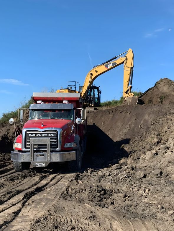 A dump truck is driving down a dirt road next to an excavator.