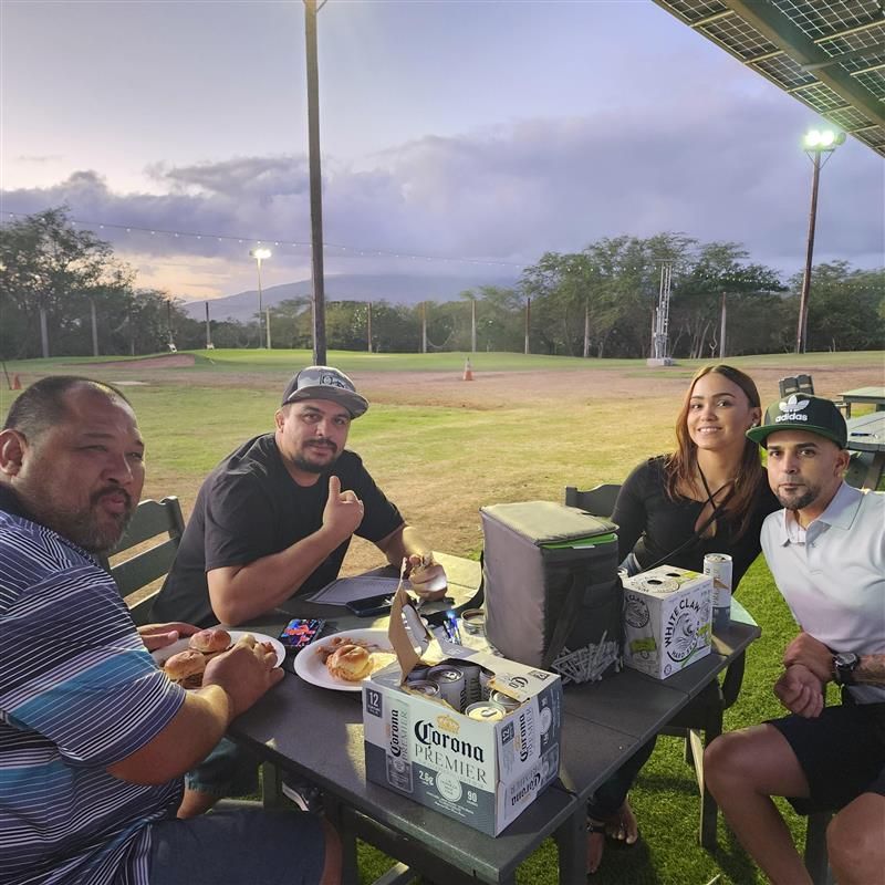 Group of friends at an outdoor table with food and drinks; smiling, relaxed, and enjoying the evening.