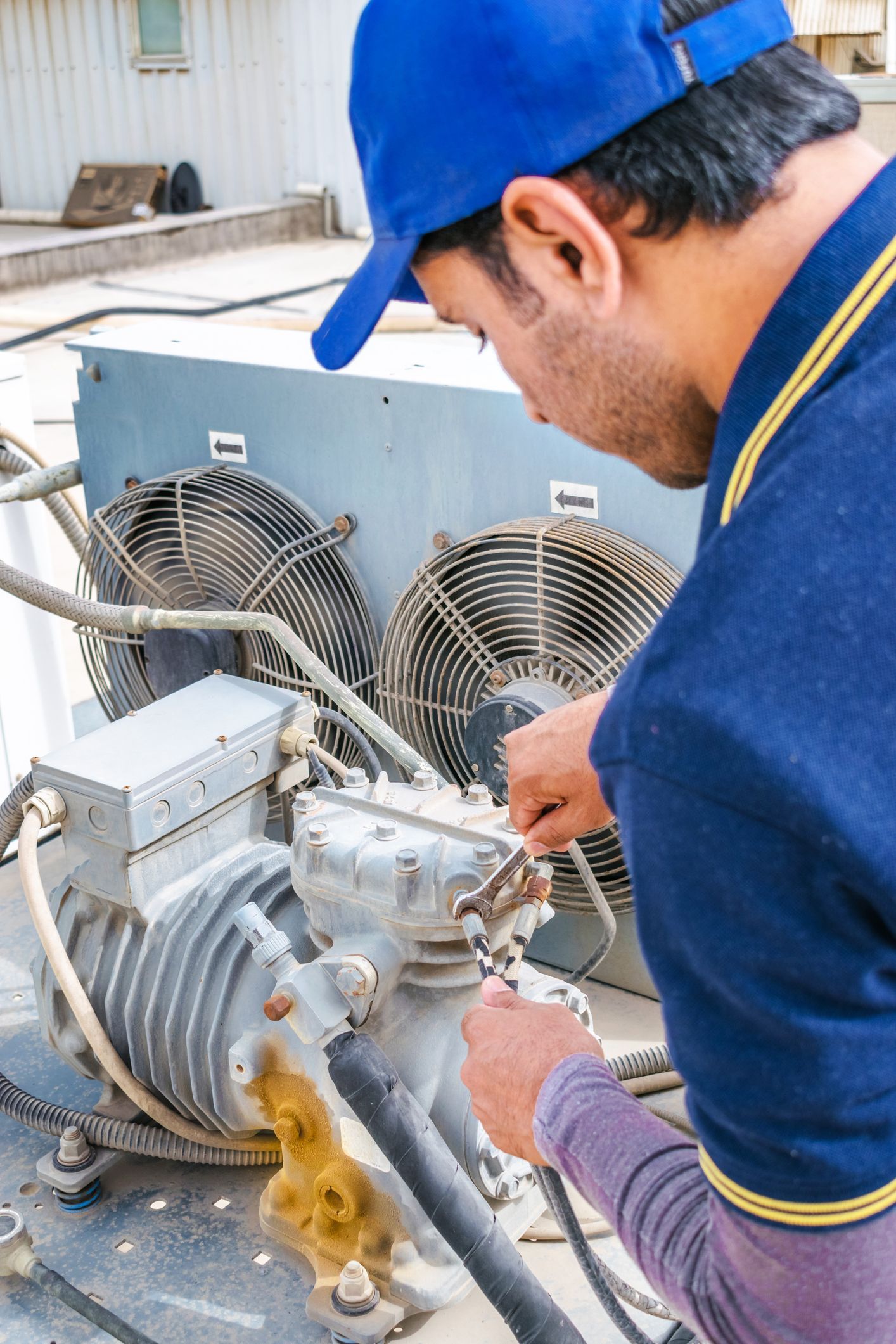 Male local electrician in blue uniform fixes heavy-duty AC unit.