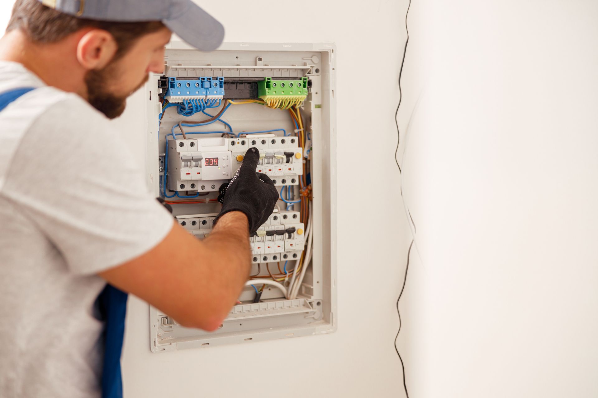 An electrical technician in uniform carefully works on a fuse switchboard with focus.