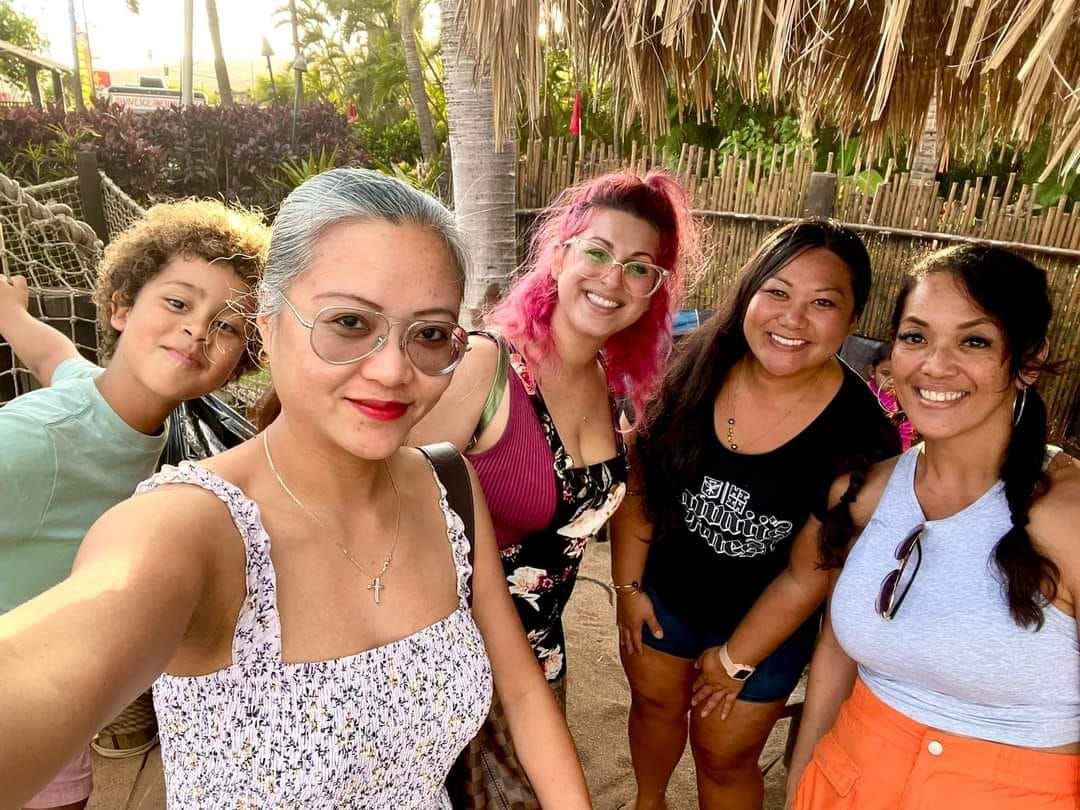 Group of five smiling people taking a selfie outdoors.  One child, three women, and one woman with pink hair.