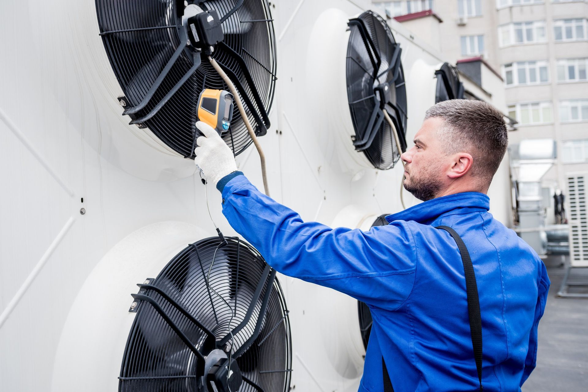 A man in a blue jacket is using a thermometer to measure the temperature of a fan.