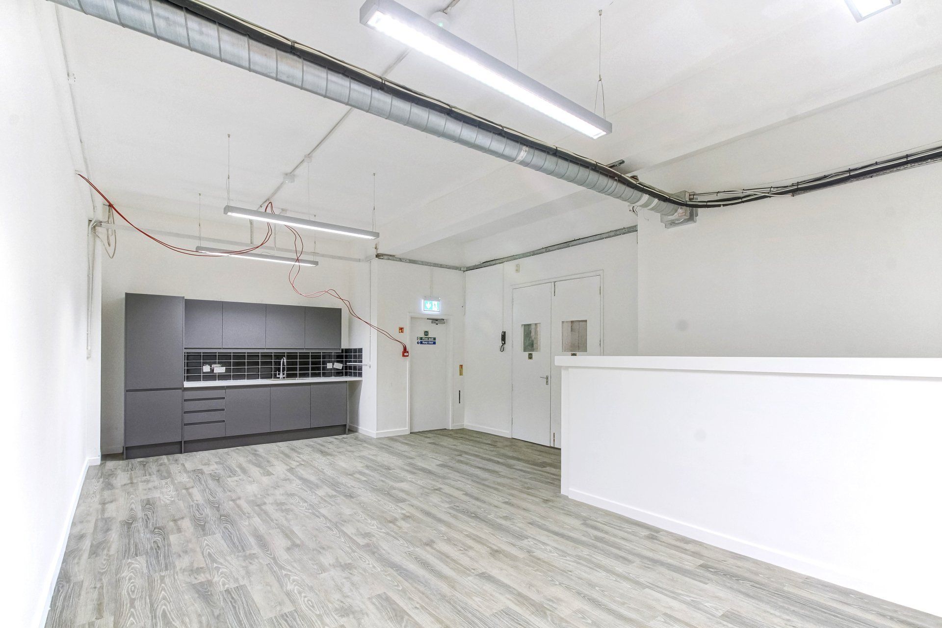 A large empty room with a wooden floor and a kitchen in the background.