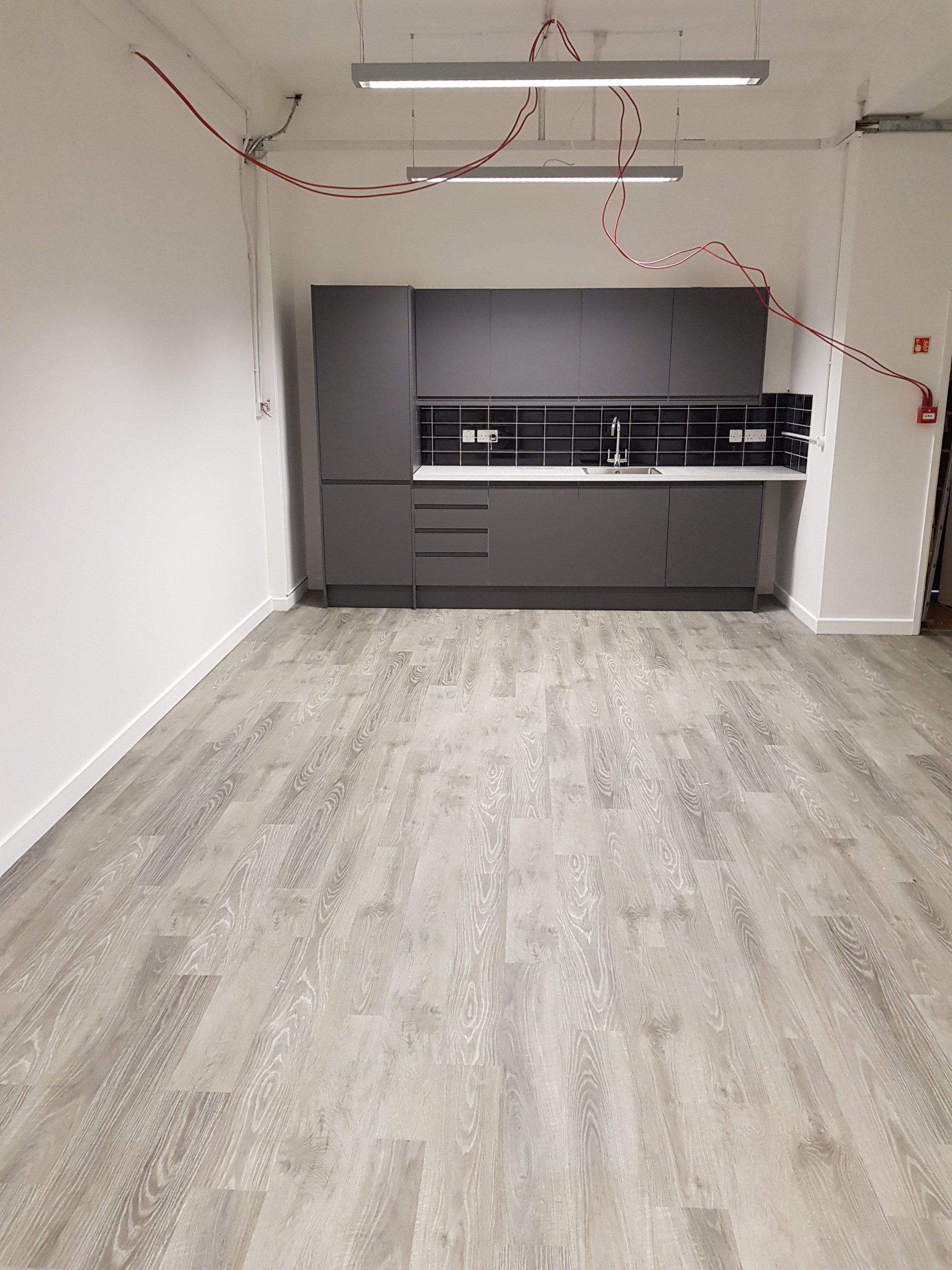 An empty room with a wooden floor and a kitchen in the background.