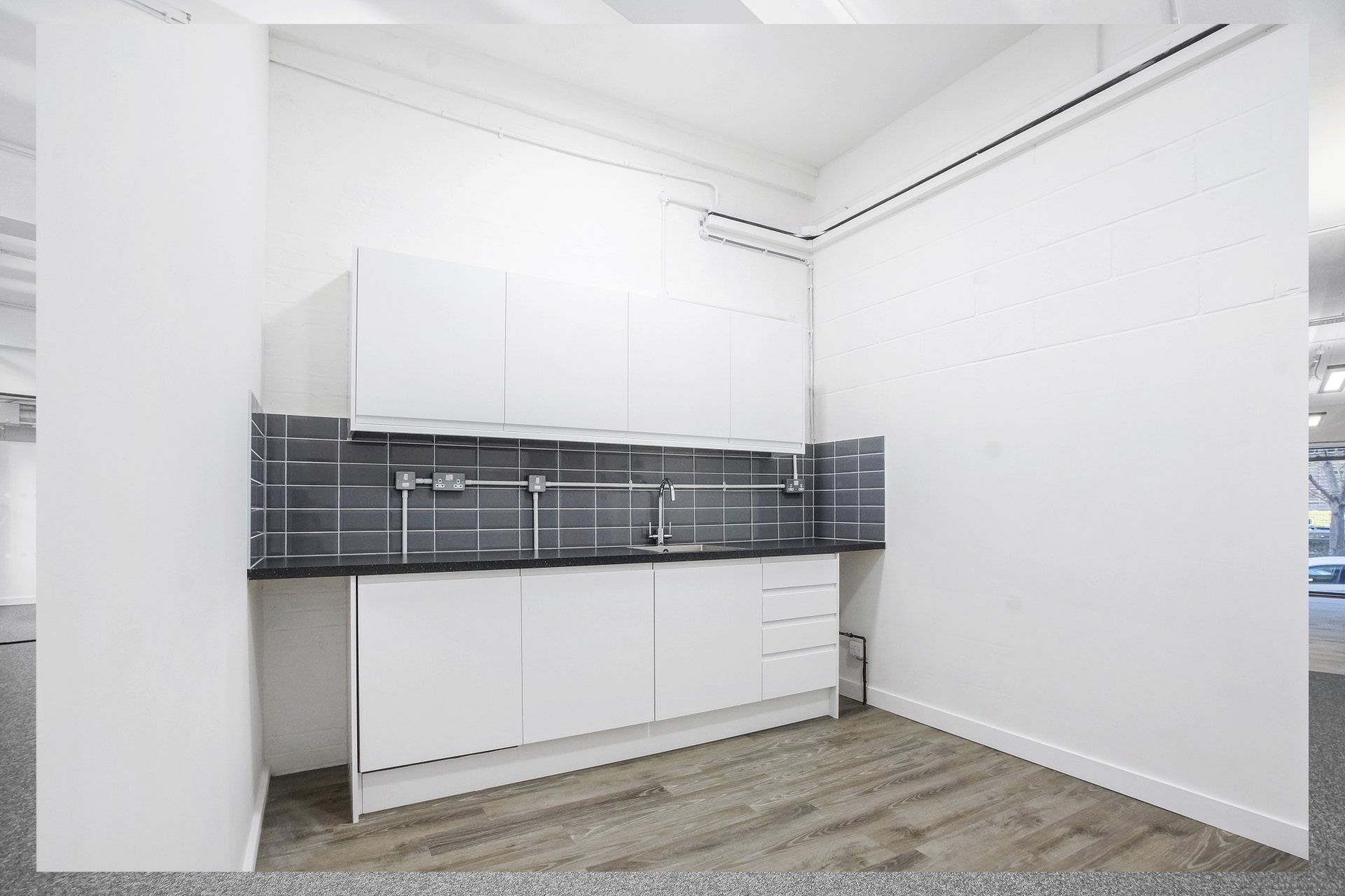 An empty kitchen with white cabinets and a sink.