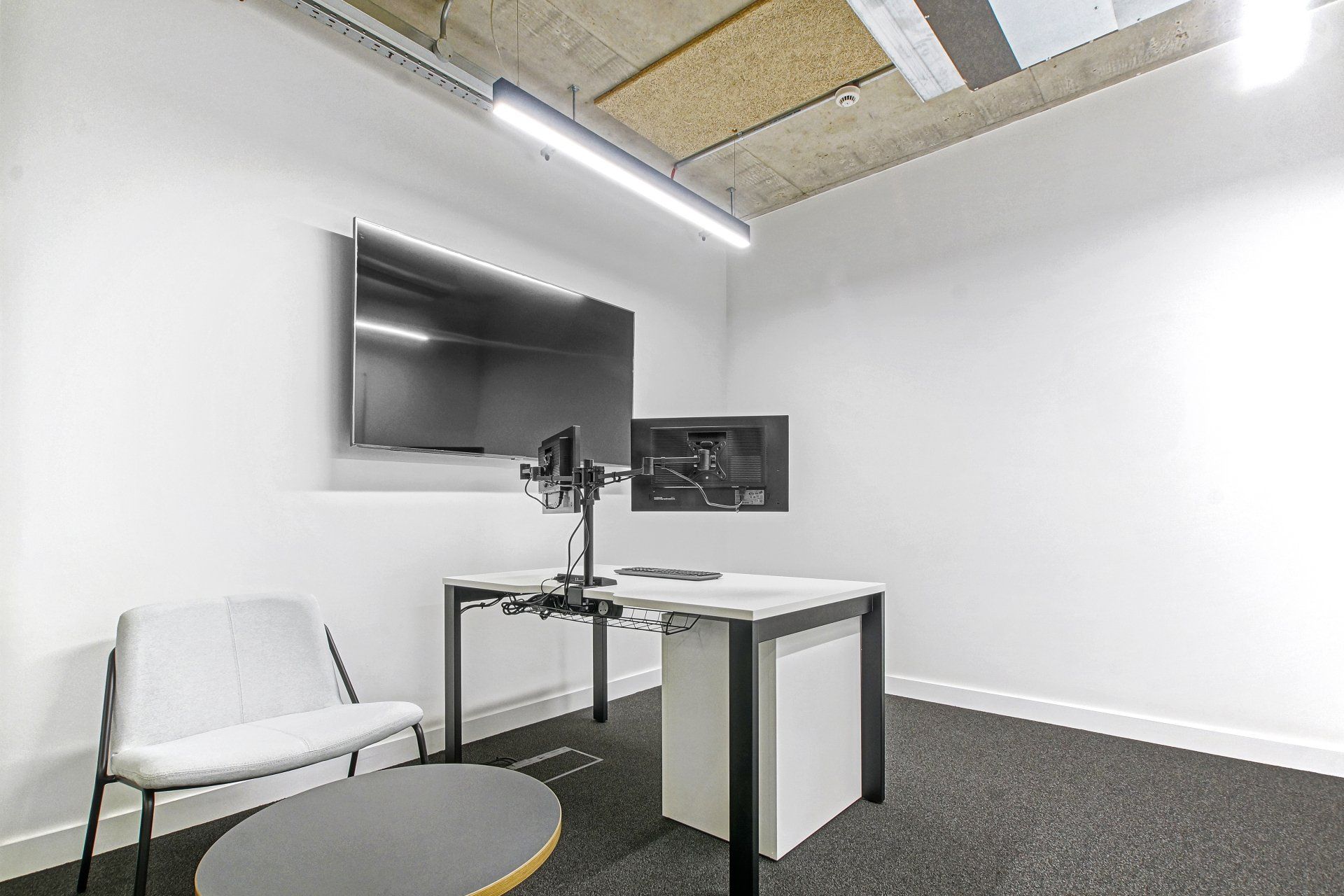 A room with a desk , chair , table and television on the wall.
