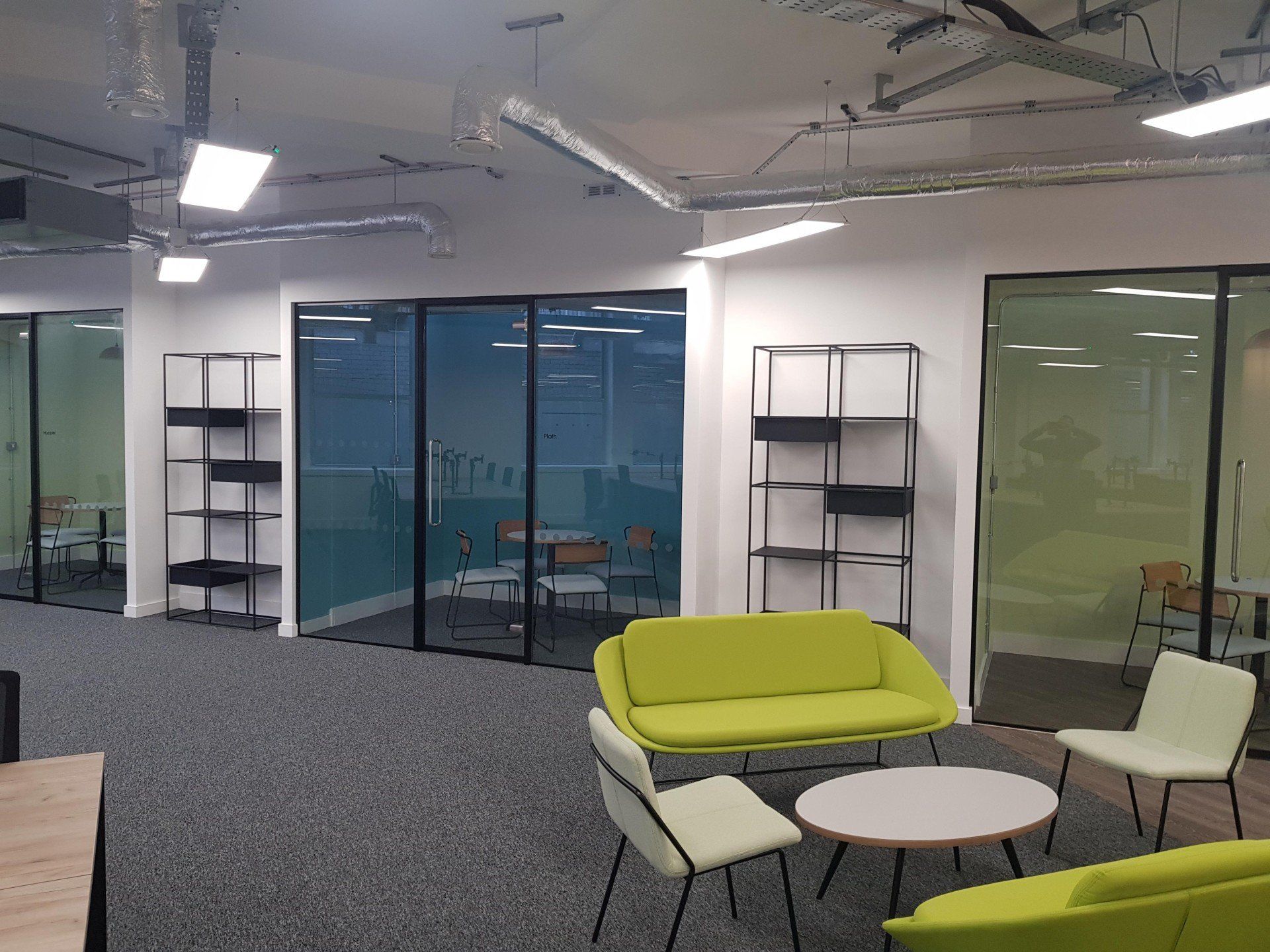 A living room with a green couch , chairs , tables and shelves.