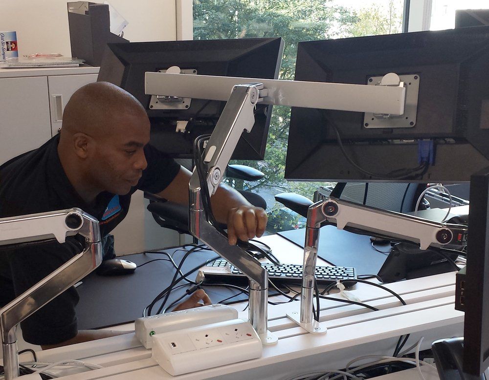 A man sits at a desk with two monitors on it