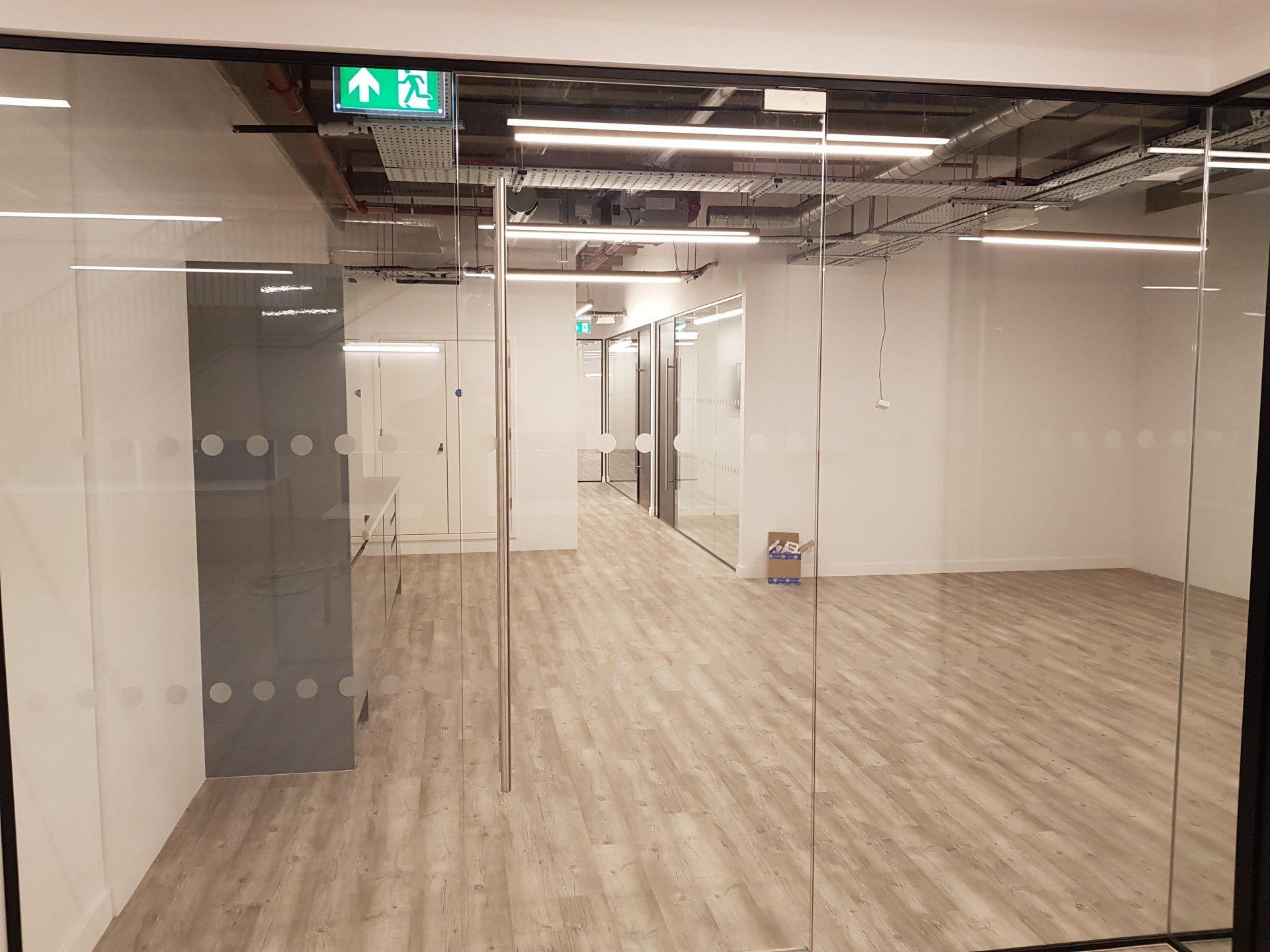 A large empty room with a green exit sign on the ceiling.