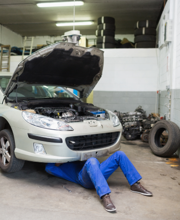 A man is laying under a car in a garage with the hood open. | Wind River Auto & Diesel