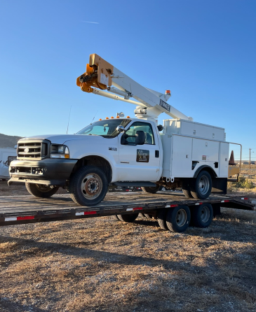 A white truck with a crane on top of it is on a trailer. | Wind River Auto & Diesel