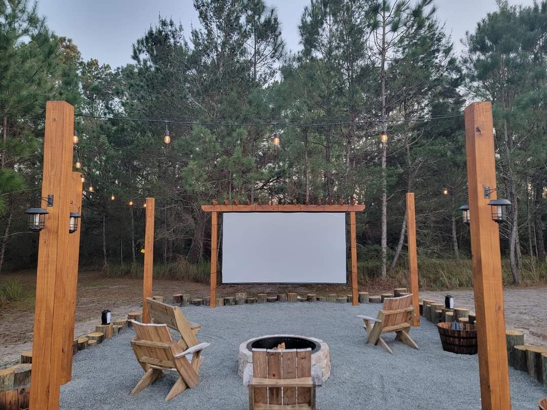 A large screen is sitting in the middle of a forest next to a fire pit.