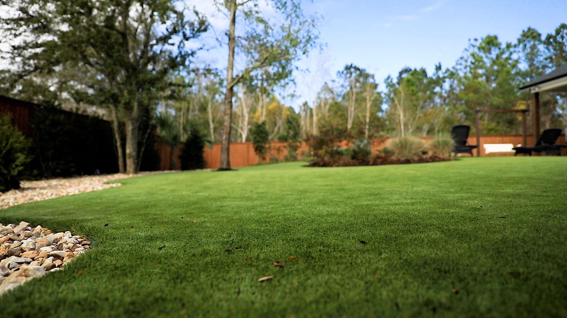 A large lush green lawn with trees in the background and a house in the background.