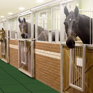 A row of horses in stables with a green floor