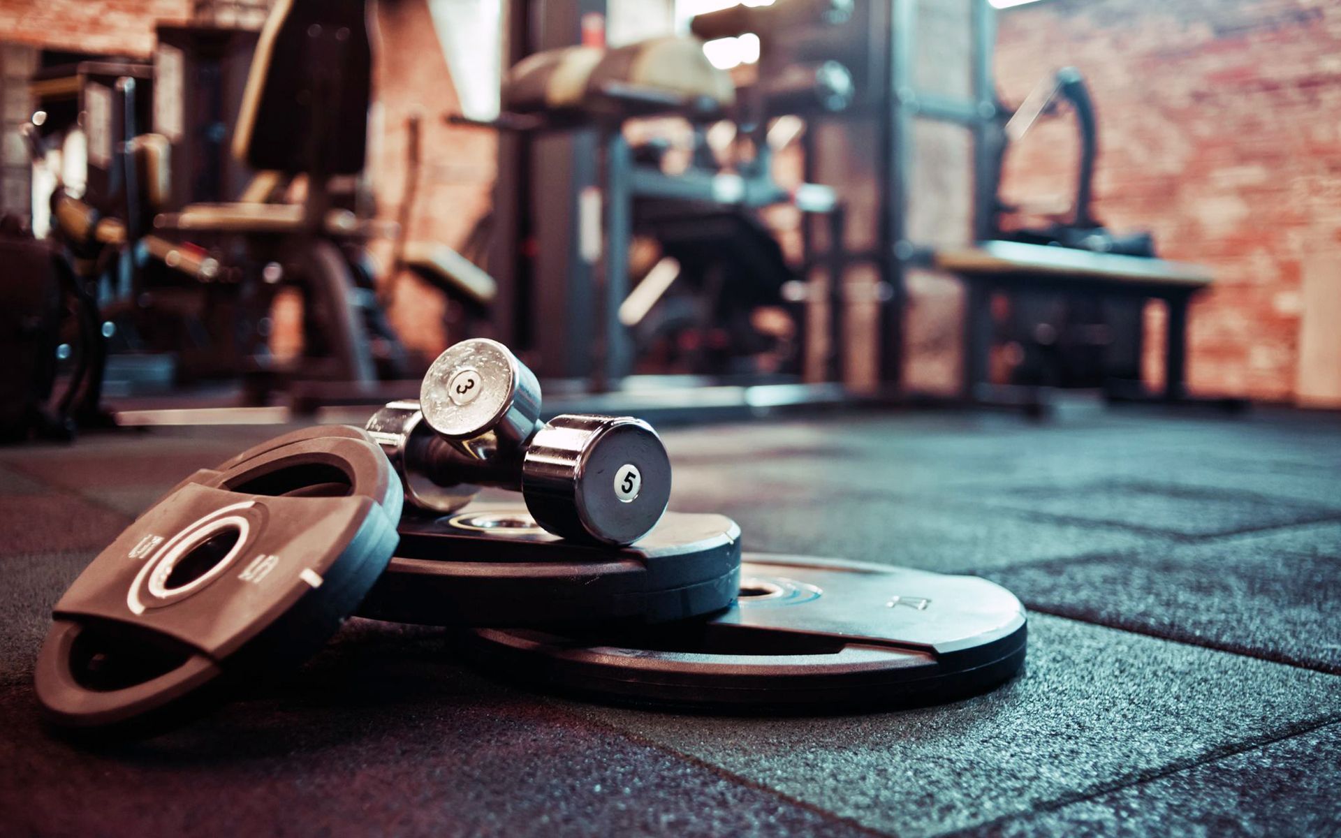 A stack of dumbbells and weight plates on the floor of a gym.