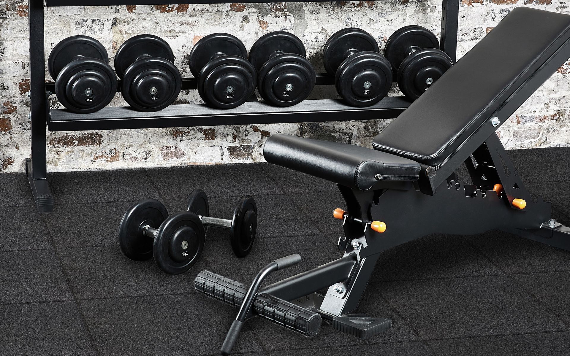 A bench and dumbbells are on the floor in a gym.