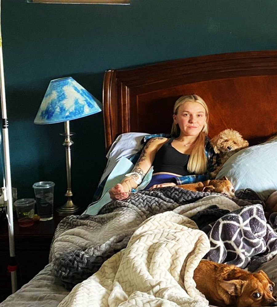 A young woman resting in bed with her pets while receiving an intravenous vitamin drip.