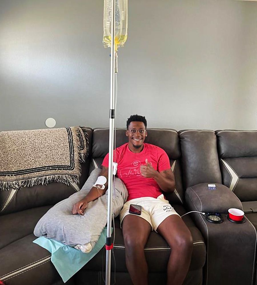 A man giving a thumbs up while receiving at-home IV hydration therapy for wellness recovery.