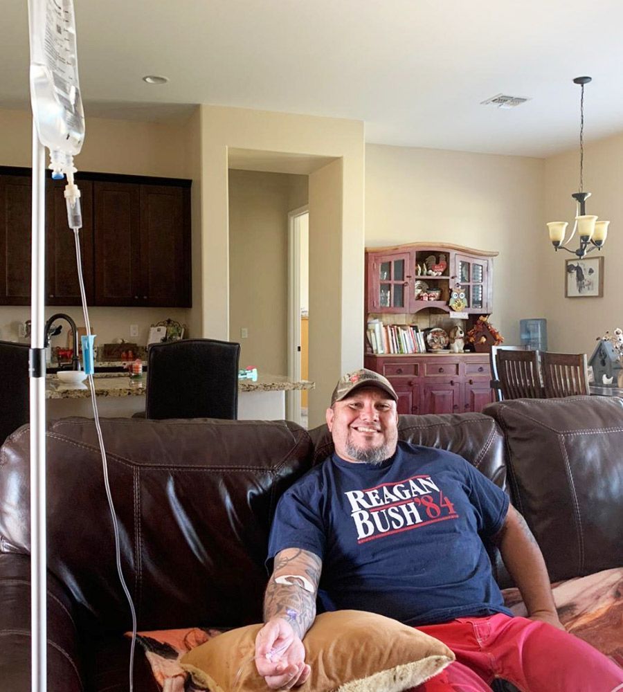 A person receiving an IV therapy treatment while relaxing on a sofa in a bright, modern living room.