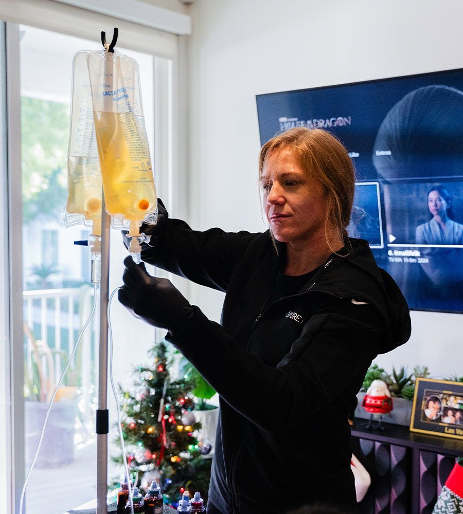 Nurse preparing customized IV vitamin infusion in a client's living room, emphasizing professional service and the ability to receive treatment while relaxing at home.